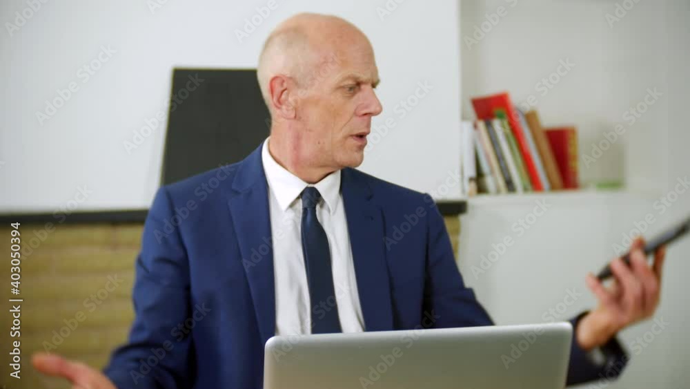 An angry mature businessman is talking on the phone in his home office. He is speaking to customer services and is frustrated and upset. An angry mature businessman is talking on the phone in his home office. He is speaking to customer services and is frustrated and upset.