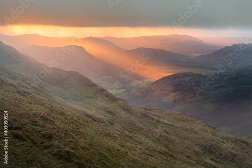 Golden evening light at sunset breaking through clouds onto mountains. Eskdale Valley in the English Lake District