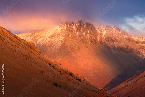 Majestical snowcapped mountains with dark dramatic clouds and red Winter light. Nature background. Lake District National Park  UK.