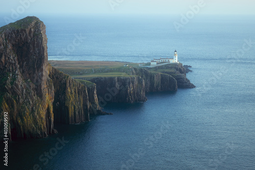 A scennery of a glowing lighthouse standing on a stunning cliff lit after sunset. Neist Point, Isle of Skye, Scotland