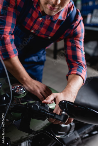 cropped view of mechanic checking start button on motorcycle handlebar, blurred foreground