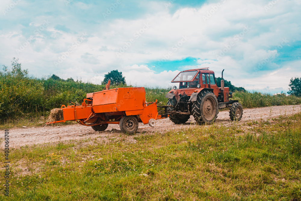 Obraz premium The process of harvesting hay for cattle, a tractor making bales in the field, old machinery.