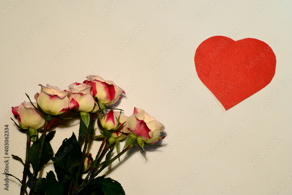 On the white surface is a bouquet of fresh flowers of roses and a red heart in the upper corner. Valentine's day postcard.