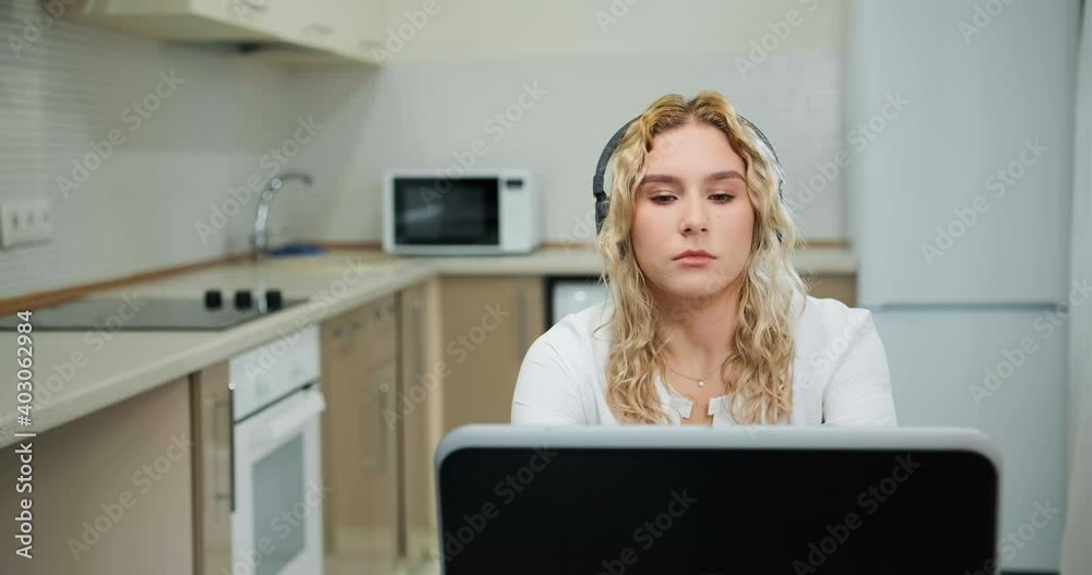 Sleepy young woman with long loose curly hair listens to online lecture holding head on hand and looking at laptop display Sleepy young woman with long loose curly hair listens to online lecture holding head on hand and looking at laptop display