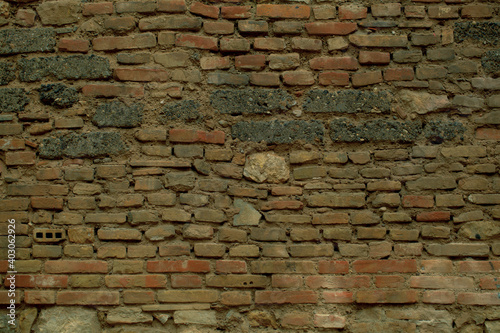 Old weathered irregular brick wall texture with exposed rows of bricks in assorted sizes and shapes in a full frame view