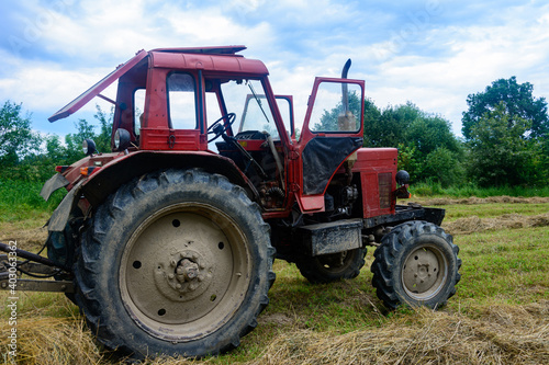 Old red tractor in the field during the haymaking season  pressing hay on bales  forage harvesting.