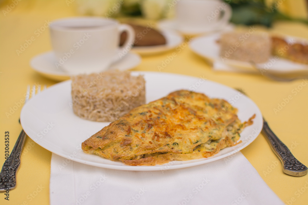 Egg omelet with chicken and cheese. Brizol with brown rice in a white ceramic bowl on a yellow tablecloth. Egg omelet with chicken and cheese. Brizol with brown rice in a white ceramic bowl on a yellow tablecloth.
