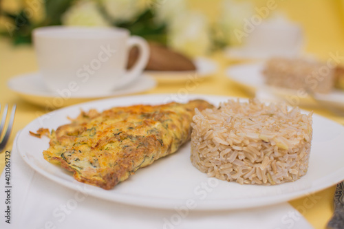 Egg omelet with chicken and cheese. Brizol with brown rice in a white ceramic bowl on a yellow tablecloth.