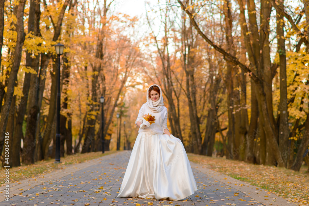 Cute girl in long white wedding dress posing in rural path among autumnal trees in golden hour. Cute girl in long white wedding dress posing in rural path among autumnal trees in golden hour.