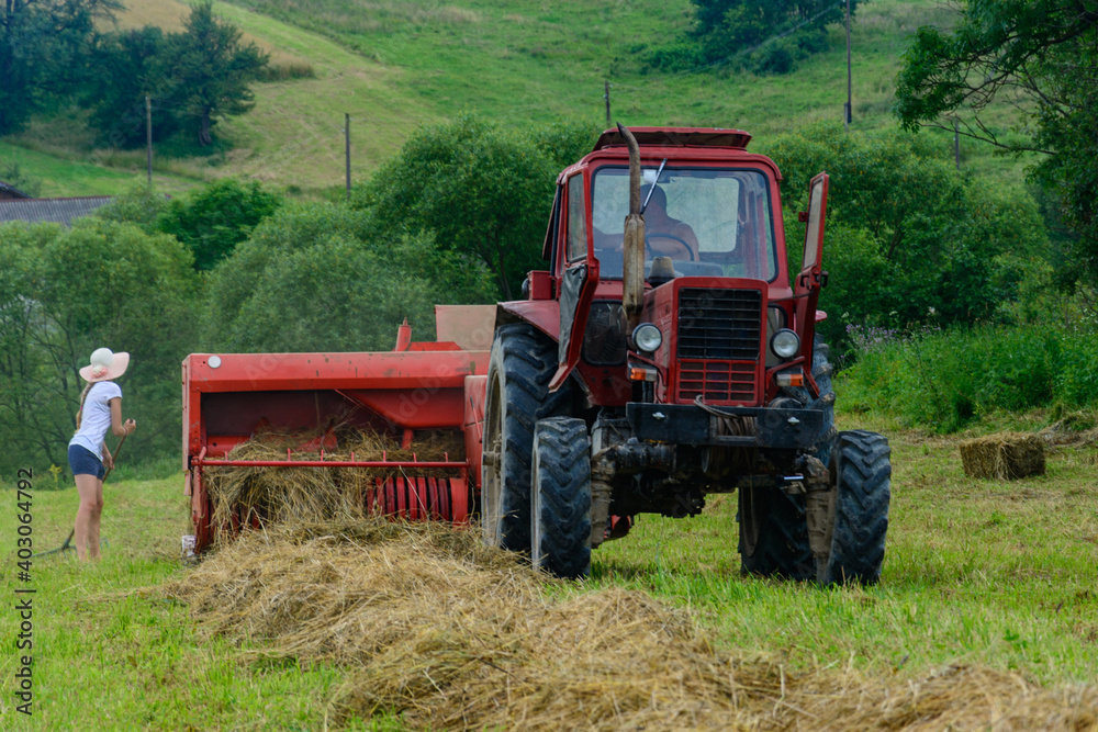Old red tractor in the field, Ukrainian fields and old machinery, hay harvesting in the field. Girl rakes the grass with a rake. Old red tractor in the field, Ukrainian fields and old machinery, hay harvesting in the field. Girl rakes the grass with a rake.