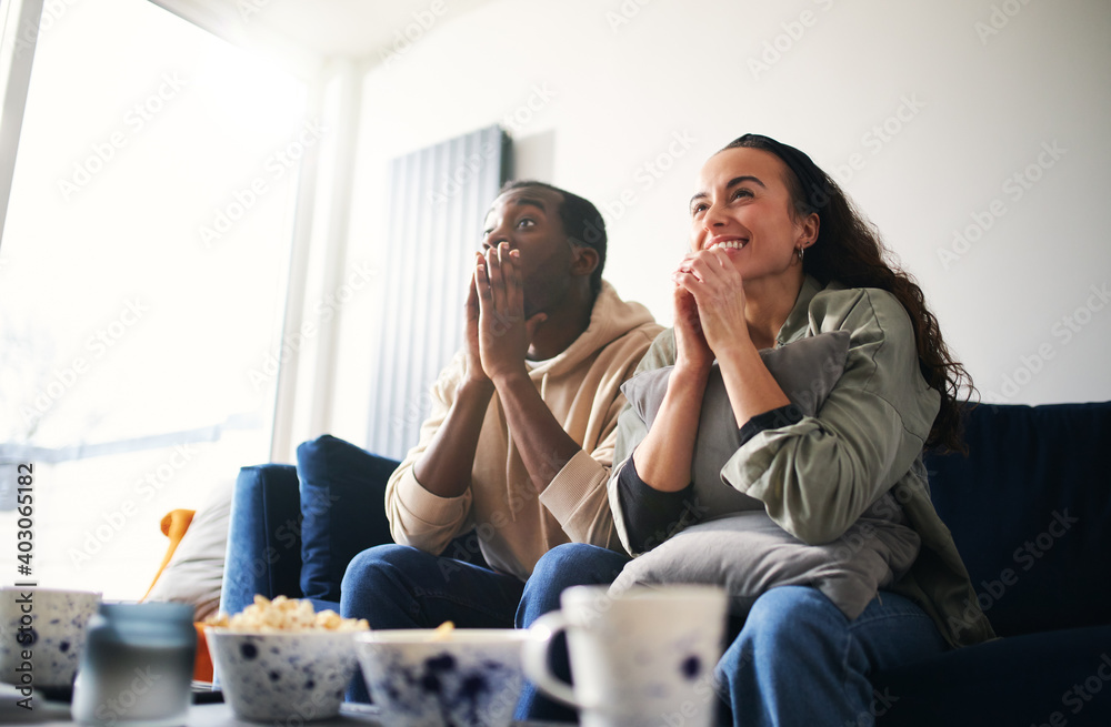 Excited Young Couple Relaxing At Home Sitting On Sofa Whilst Watching Sport On TV Together Excited Young Couple Relaxing At Home Sitting On Sofa Whilst Watching Sport On TV Together