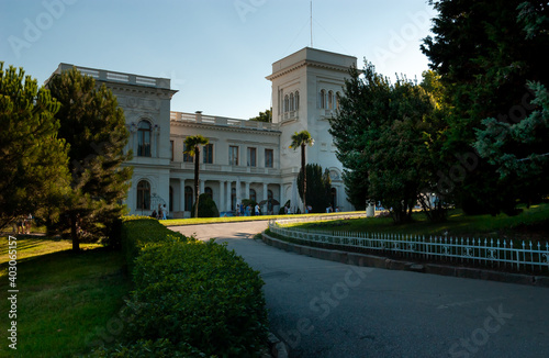 An Italian-style palace surrounded by park greenery. Evening sun, long shadows. White facade in the shade against the blue sky. Crimea, Livadia Palace, in the early 20th century. photo