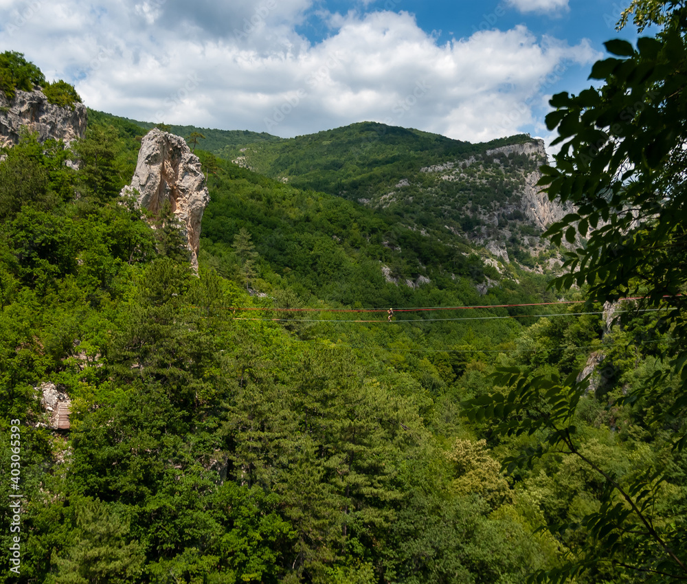 Obraz premium A climber at a high altitude above the mountain slopes overgrown with forest. Constructs a cableway over the great Crimean canyon. Crimea.