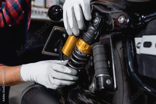 cropped view of mechanic checking shock absorber of motorcycle in workshop