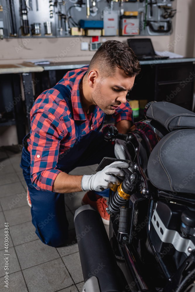 young mechanic in plaid shirt checking shock absorber of motorbike in workshop young mechanic in plaid shirt checking shock absorber of motorbike in workshop