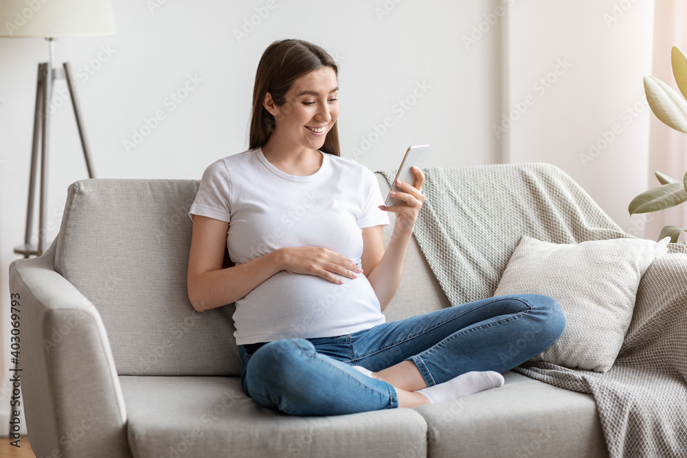 Happy pregnant millennial woman using smartphone at home, browsing pregnancy app Happy pregnant millennial woman using smartphone at home, browsing pregnancy app