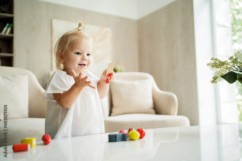 beautiful baby girl playing at home alone with her children's colored toys for development. on the table in the living room. Blonde of European appearance beautiful baby girl playing at home alone with her children's colored toys for development. on the table in the living room. Blonde of European appearance