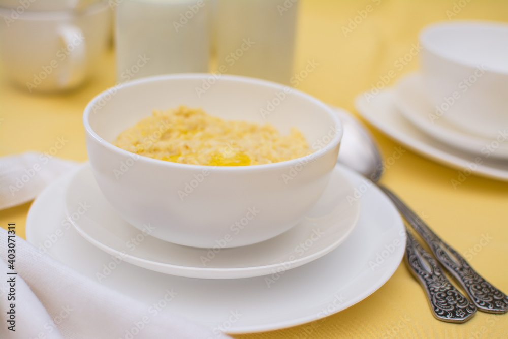 Millet porridge with butter in a white ceramic cup on a yellow tablecloth. Healthy eating. Healthy breakfast. Millet porridge with butter in a white ceramic cup on a yellow tablecloth. Healthy eating. Healthy breakfast.