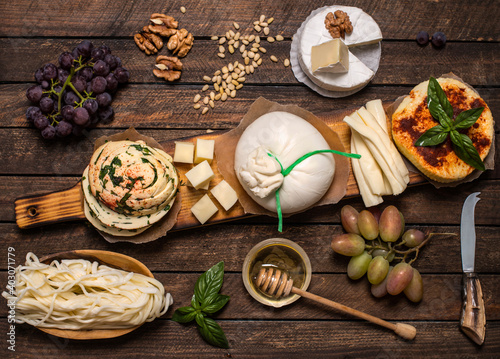 A set of cheeses. Halumi, cheese sticks, Suluguni, Camembert, fresh soft white burrata cheese ball, mozzarella on a wooden board. Top view. Cheese board with nuts and grapes. Various types of cheese.
