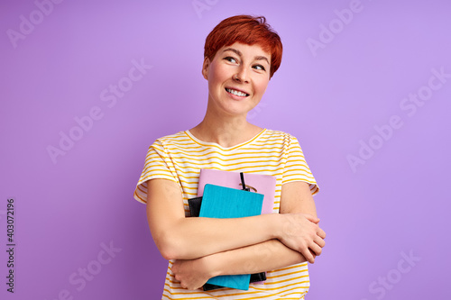 female holds books in hands andlooking at side, isolated over purple background. young redhead female enjoy studying, education photo