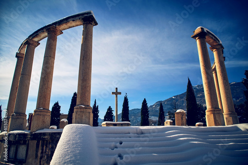 Snowy italian cemetery with colonnade and cross in the center