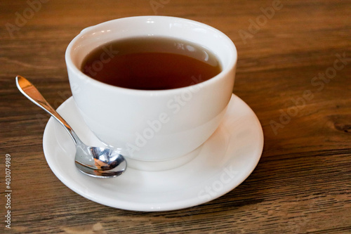 white cup of tea on plate with teaspoon on wooden table in cafe