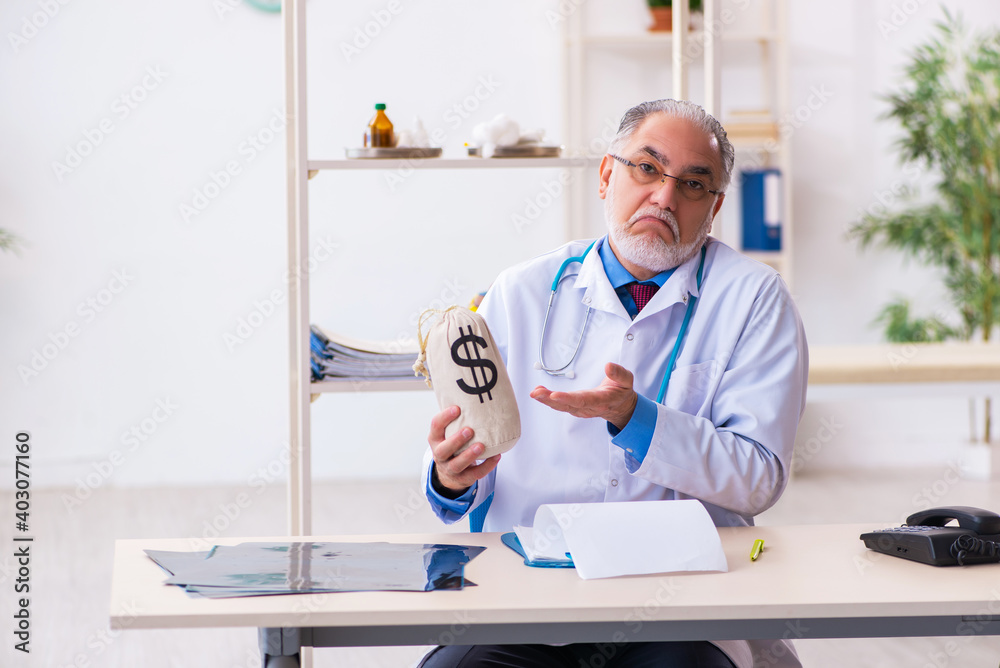 Old male doctor holding moneybag in the hospital