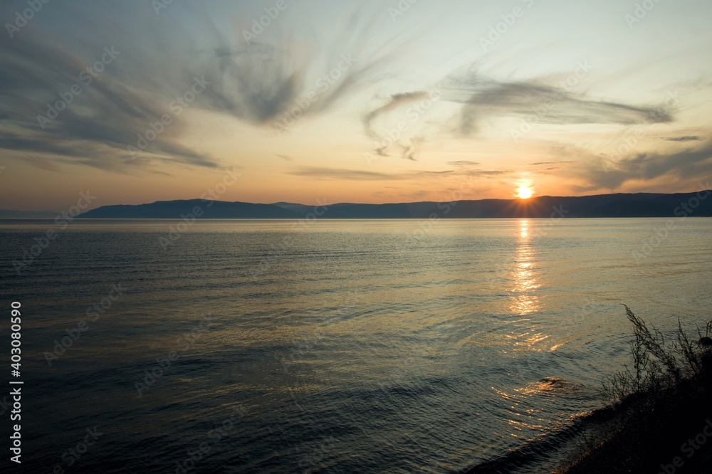 Sunset on Baikal lake with sun setting down behind the mountain and sun rays