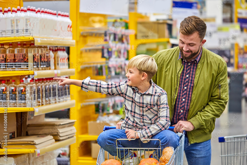 boy enjoys shopping time with father in supermarket, handsome guy carry son on a cart, have fun