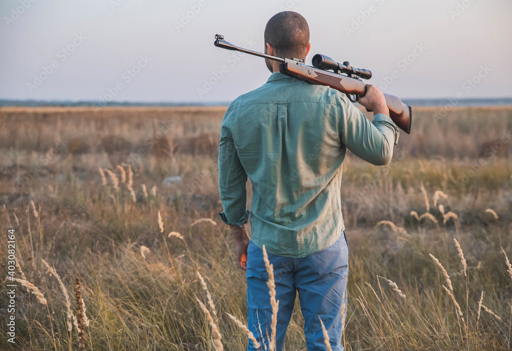 Fototapeta premium hunter stands in the field with his back putting the gun on his shoulder