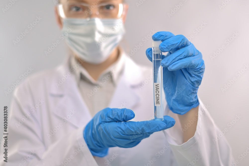 Close-up view of microbiologist in protective blue gloves and face mask holds biological tube with vaccine on white background. Backstage of scientific discovery. Healthcare and medicine concept. Close-up view of microbiologist in protective blue gloves and face mask holds biological tube with vaccine on white background. Backstage of scientific discovery. Healthcare and medicine concept.