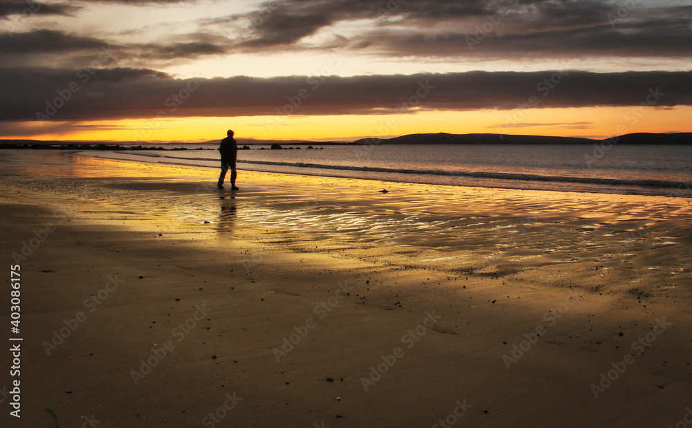Beautiful morning orange sunrise with silhouetted man walking down the Silverstrand beach in Galway, Ireland 