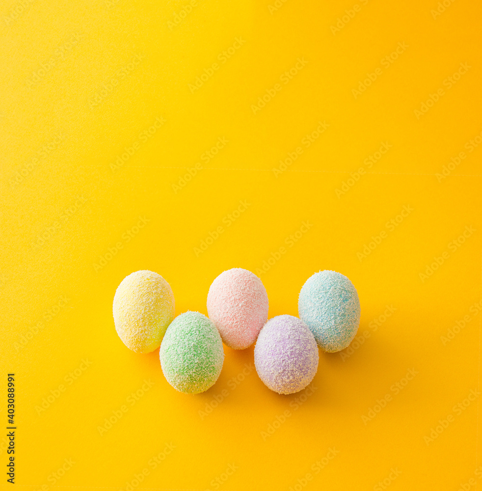 Colorful stacked up easter eggs on a bright yellow gold background. Creative minimal spring art.