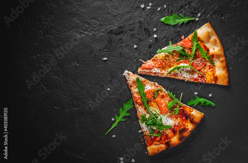 Slices of pizza with prosciutto and rocket salad with spices on black  background. Pizza is cooking in the oven. Pizza menu. View from above.  Space for text. #242342466 - Do Kuchni - FotoNaklejki