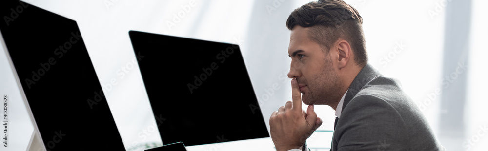 side view of concentrated trader near monitors with blank screen, banner side view of concentrated trader near monitors with blank screen, banner