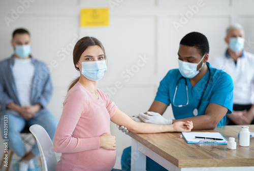 Pregnant woman in face mask getting vaccinated against Covid-19 at clinic