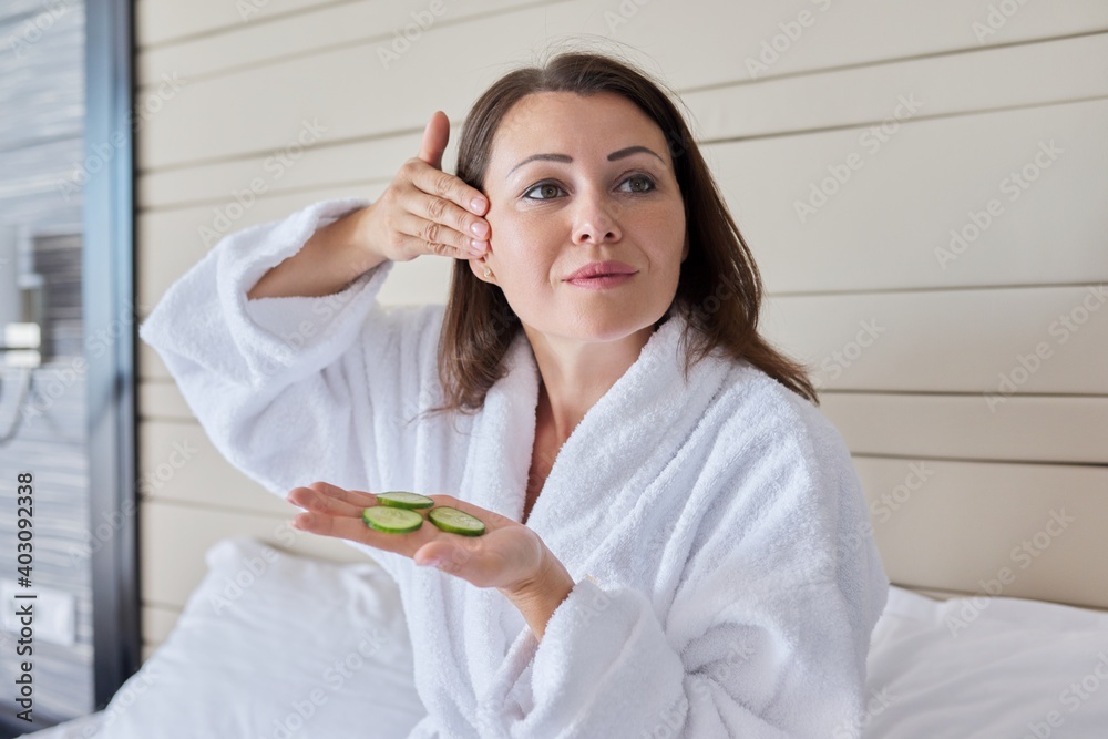 Mature female in bathrobe doing home spa treatments with cucumbers Mature female in bathrobe doing home spa treatments with cucumbers
