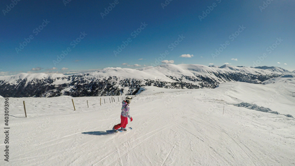 A snowboarding woman in pink outfit going down the ski run in Innerkrems, Austria. Everything is covered with fresh, powder snow. High mountains in the back. Winter outdoor activities. Free ride