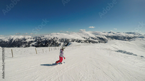 A snowboarding woman in pink outfit going down the ski run in Innerkrems, Austria. Everything is covered with fresh, powder snow. High mountains in the back. Winter outdoor activities. Free ride