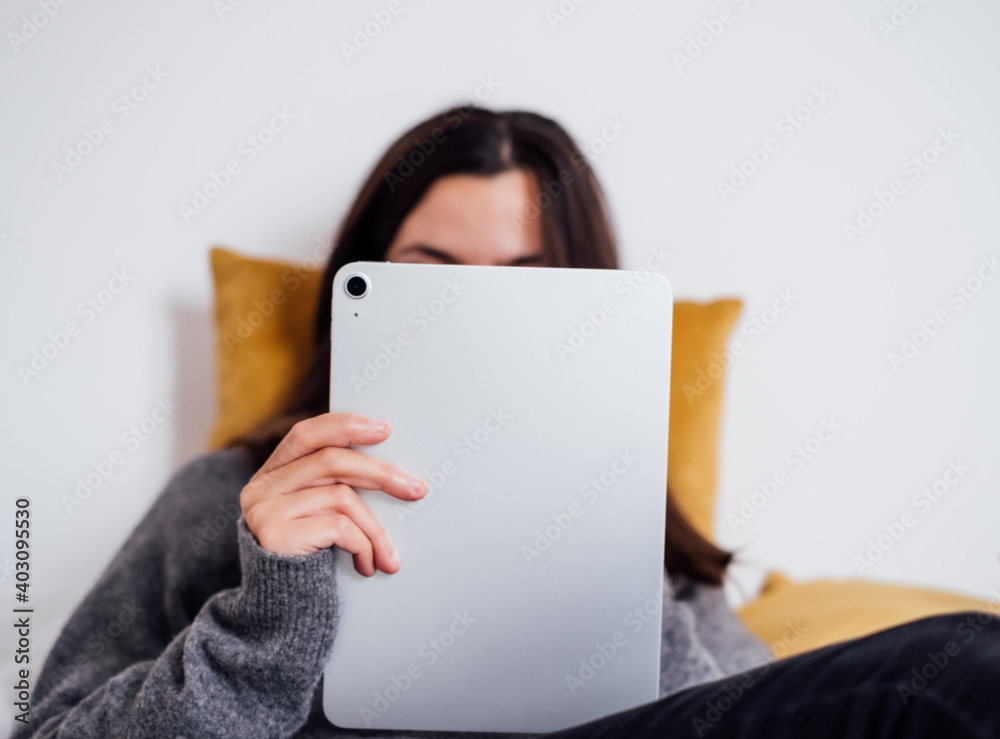 Unrecognizable woman using a silver digital tablet and lying on a bed Unrecognizable woman using a silver digital tablet and lying on a bed