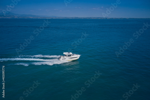 Drone view of a boat sailing at high speed. Aerial view of a yacht in motion on blue water. In the background mountains, coastline. © Berg