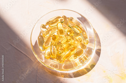 Cod liver fish oil capsules in glass bowl on pink background. Omega 3, Vitamin E supplements. Sunlight and shadows trendy shot. Healthy diet concept. Top view, close up, copy space