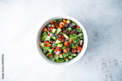 Green lentil red bell pepper cucumber parsley salad in a bowl