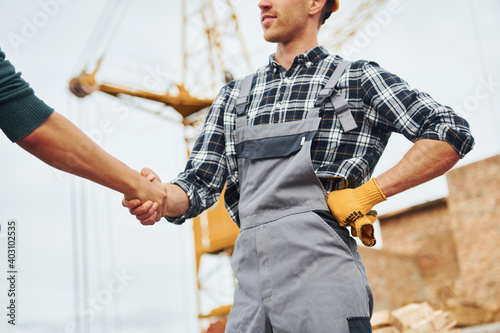 Making handshake. Two construction workers in uniform and safety equipment have job on building together photo
