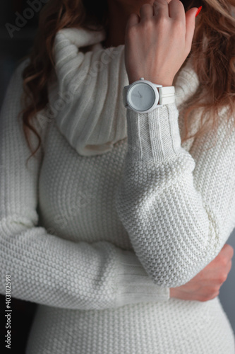 Women's white wristwatch with leather strap on the hand against the background of a white knitted sweater