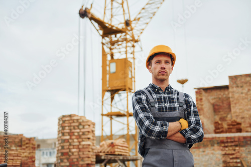 With arms crossed. Construction worker in uniform and safety equipment have job on building