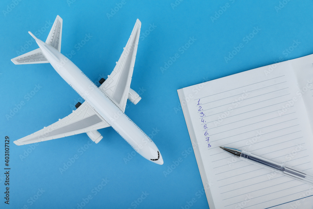 flight planning concept. plane, diary and pen on a blue background. list of things for the trip. 