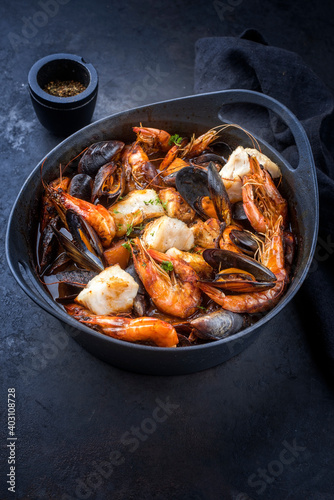 Traditional French seafood bouillabaisse with fish, king prawns and mussels in red wine sauce as close-up in a modern design pot with copy space
