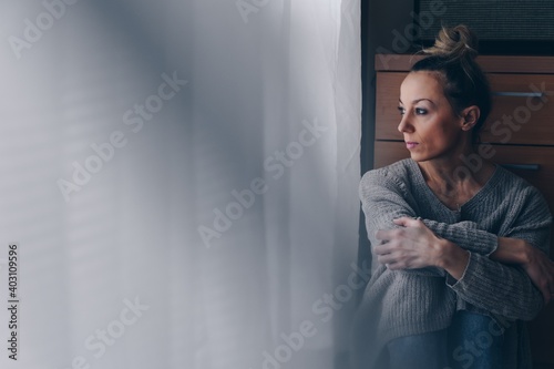 Fotografia Beautiful sad woman sitting on the floor looking at the window