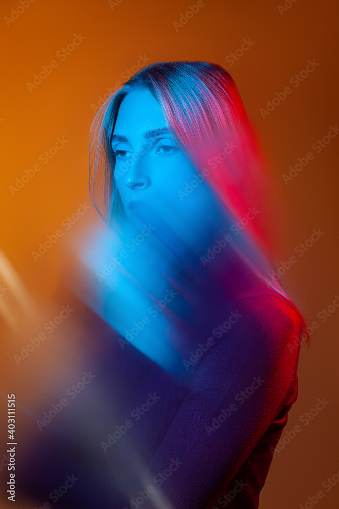 Thoughtful young lady with blue light on face in orange studio